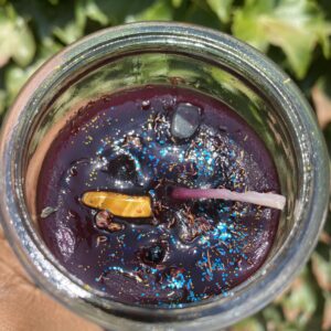 A candle in a glass jar with some purple stuff inside