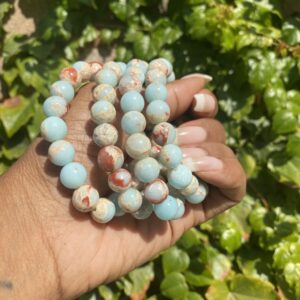 A hand holding a string of beads in front of some bushes.