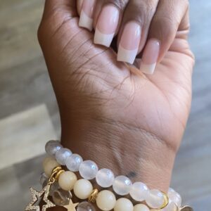 A hand with french manicure and gold star charms on it.