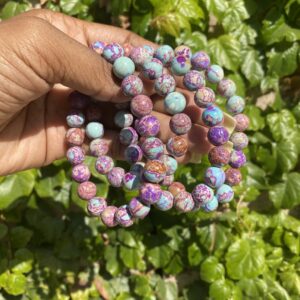 A hand holding a string of beads in front of some bushes.