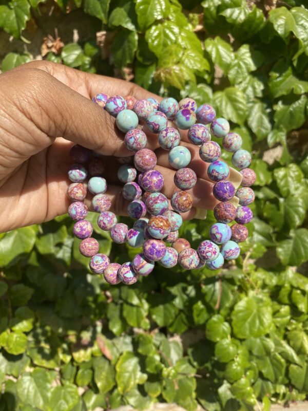 A hand holding a string of beads in front of some bushes.