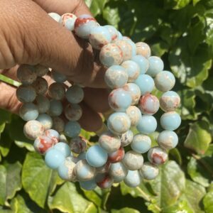 A hand holding a string of beads in front of some plants.