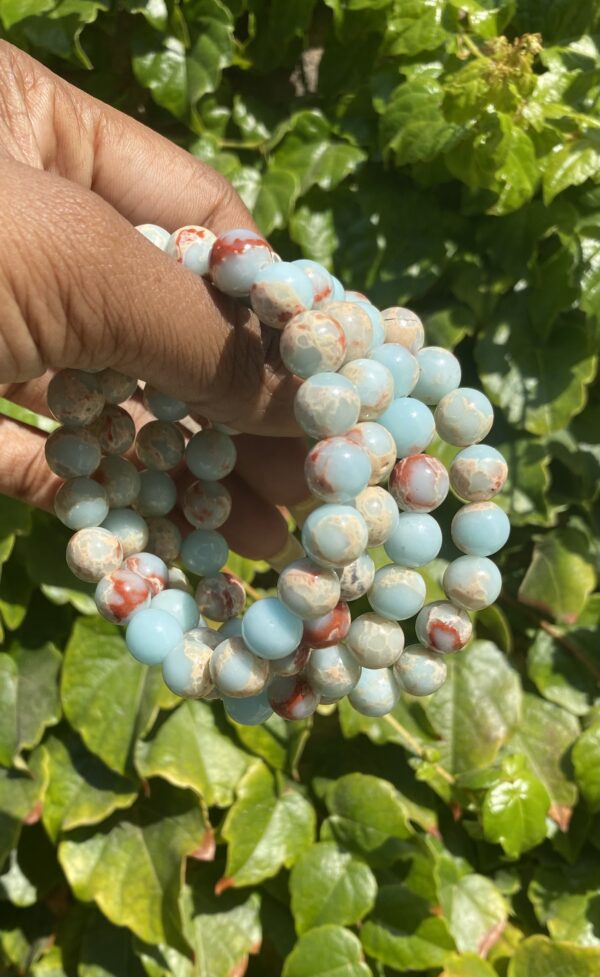 A hand holding a string of beads in front of some plants.