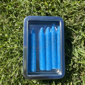 A tin of blue candles sitting on the grass.