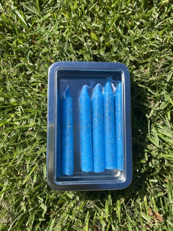 A tin of blue candles sitting on the grass.