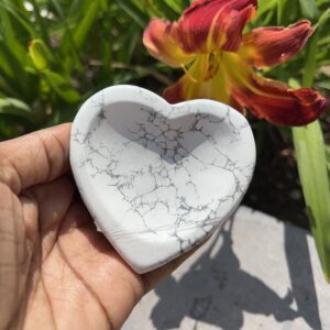 A person holding a heart shaped dish in front of some flowers.