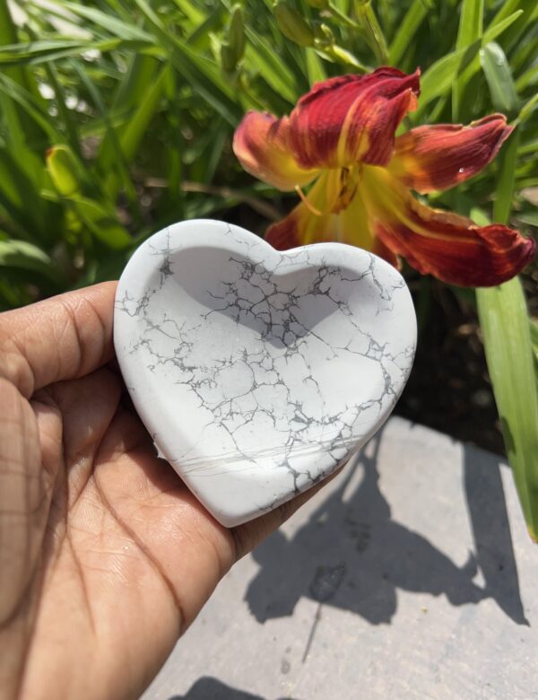 A person holding a heart shaped dish in front of some flowers.