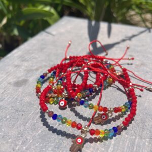 A stack of bracelets with red string and evil eye charms.