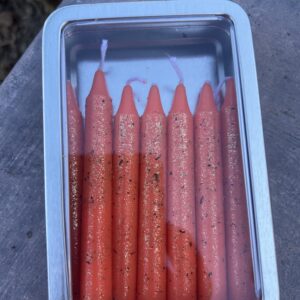 A tin of candles with orange wax.