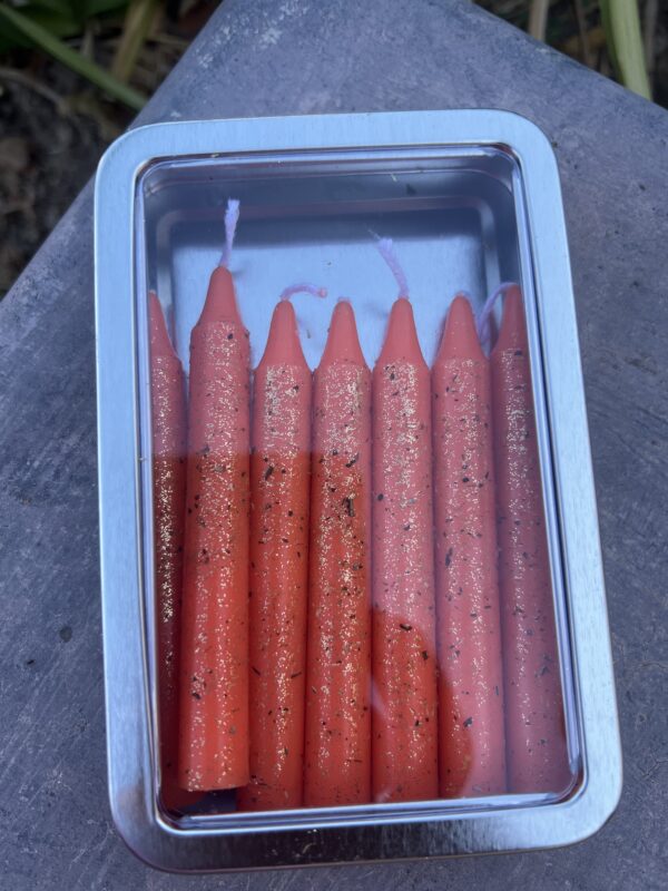 A tin of candles with orange wax.