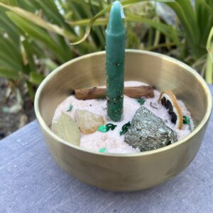 A candle in the middle of a bowl with rocks and plants.