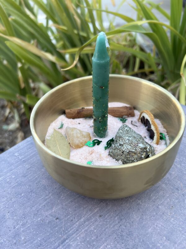 A candle in the middle of a bowl with rocks and plants.