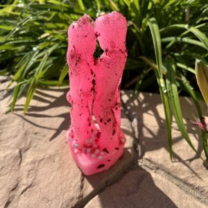 A pink candle sitting on the ground next to some grass