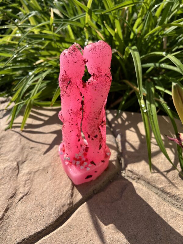 A pink candle sitting on the ground next to some grass