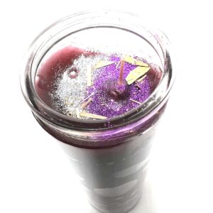 A purple candle in a glass on top of a table.