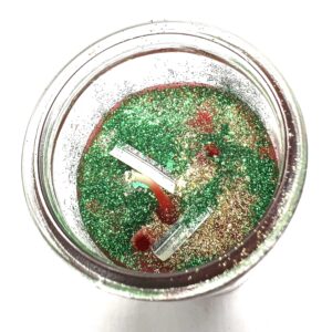 A jar of green and red sand with two white sticks in it.