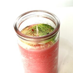 A candle in a jar with pink liquid and green leaves.