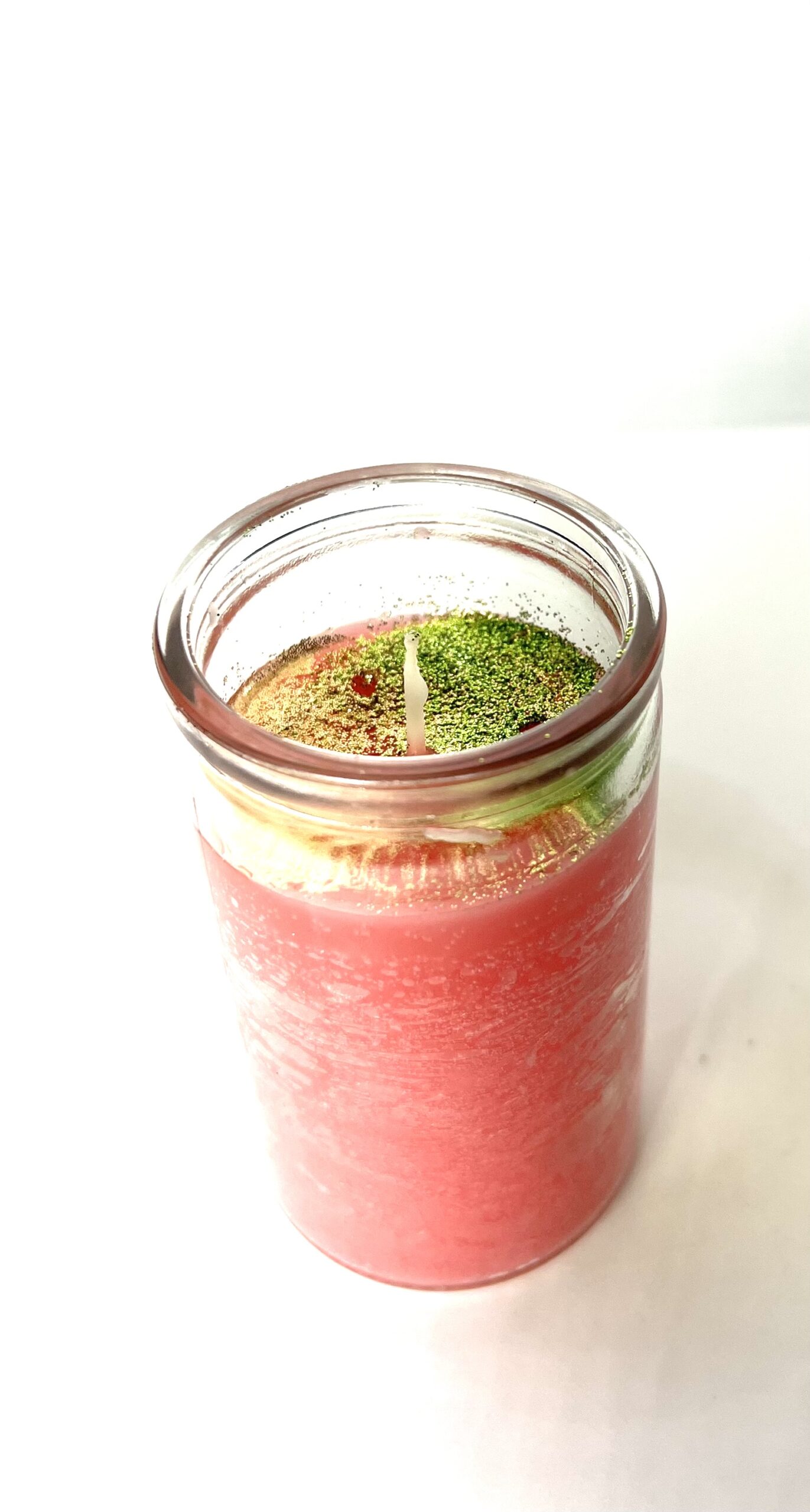 A candle in a jar with pink liquid and green leaves.