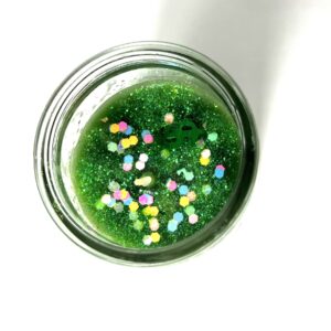 A jar of green liquid with sprinkles in it.