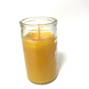 A candle in a glass is lit and has an orange.