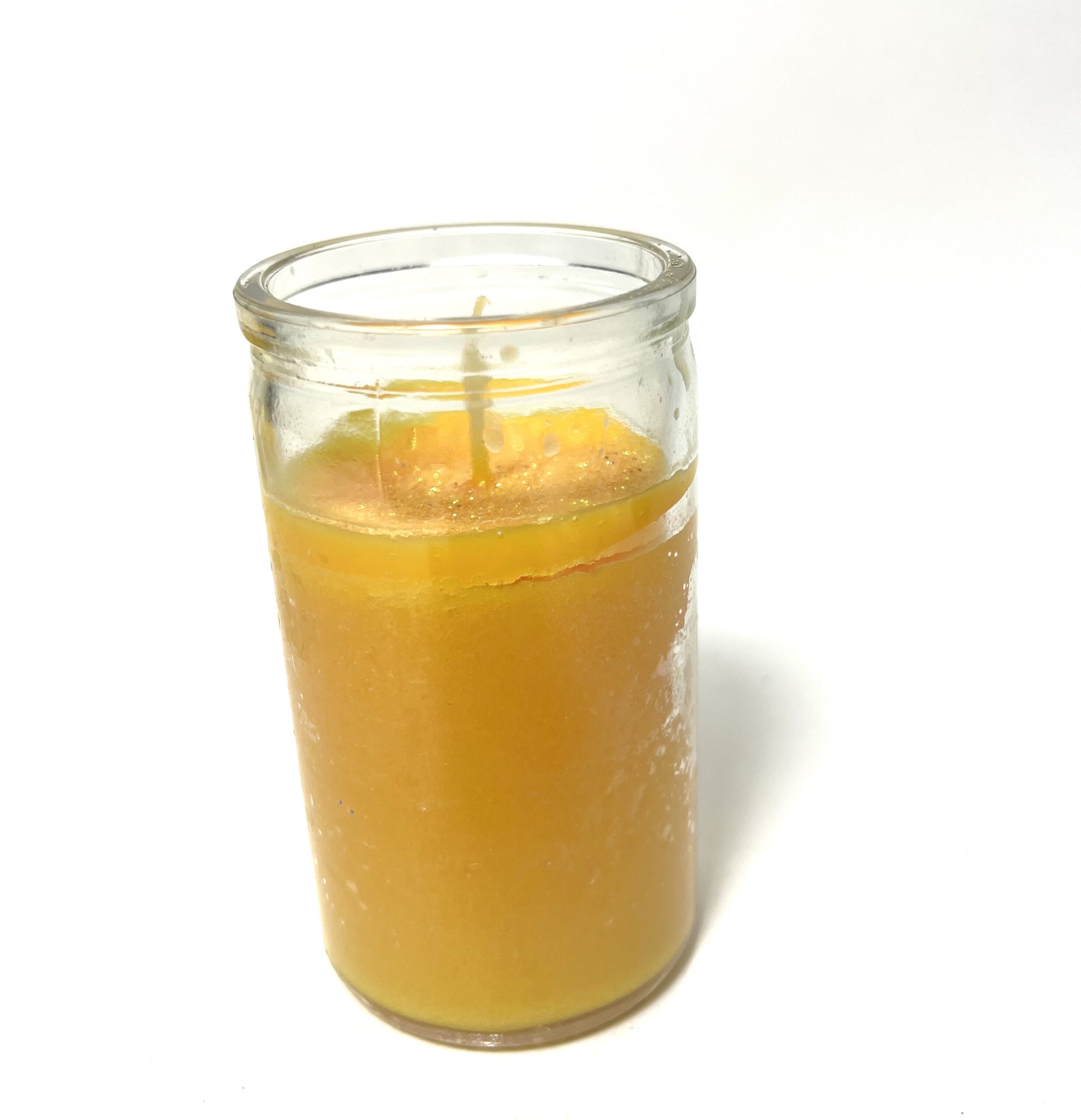 A candle in a glass is lit and has an orange.