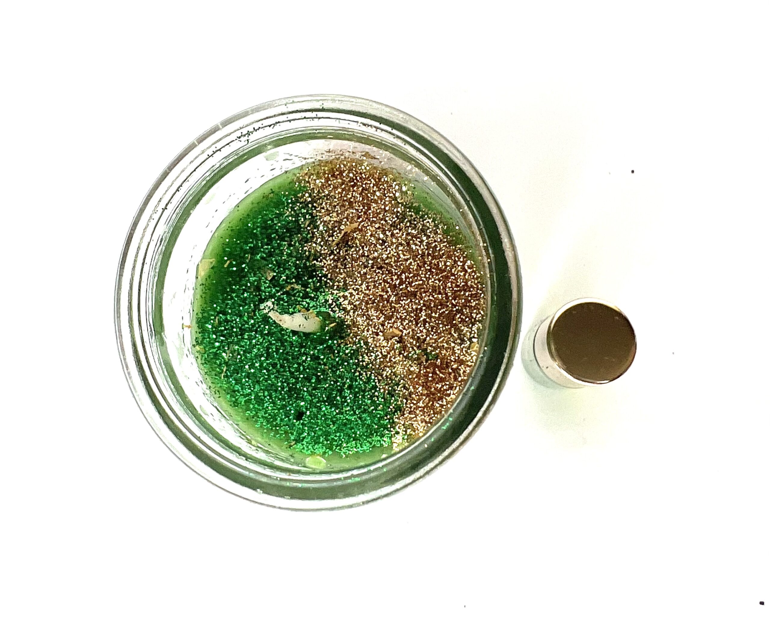 A jar of green and brown sand next to a bottle.